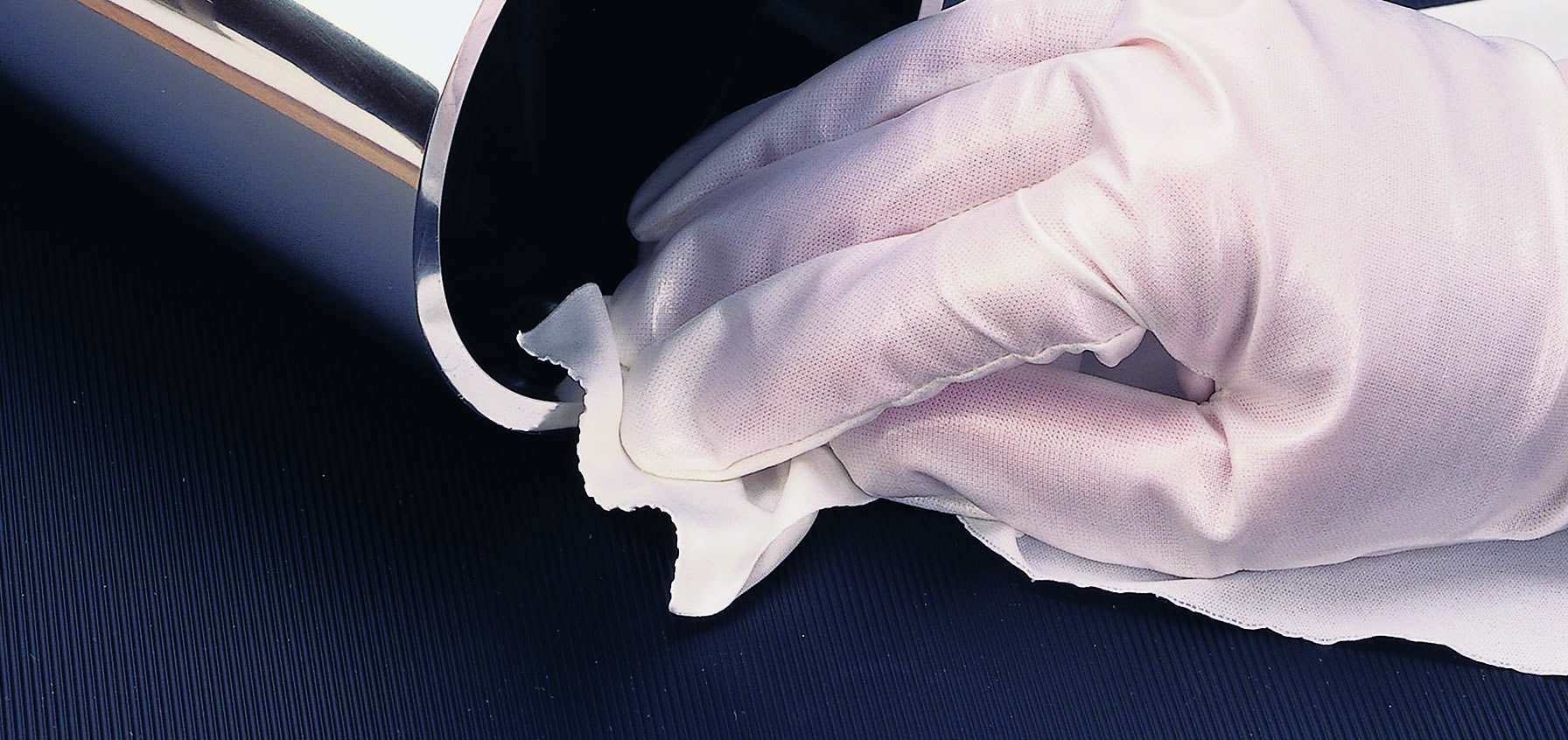 A hand wearing sterile gloves cleaning a metal tube with a cleanroom wipe